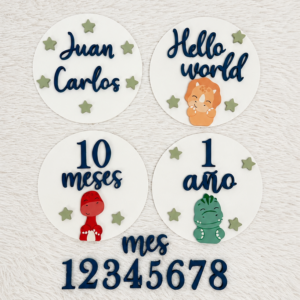 White circular milestone plaques with blue script text saying 'Juan Carlos', 'Hello world', '10 meses', and '1 ano', plus small green stars and cute cartoon figures on a soft background.